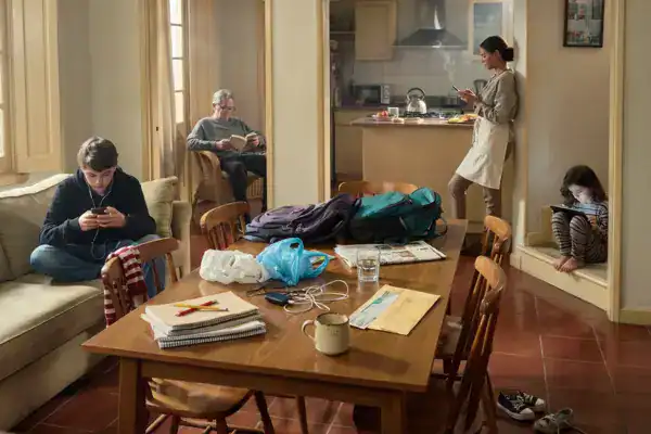 Organização de uma sala de estar com pessoas usando dispositivos móveis e objetos espalhados na mesa.